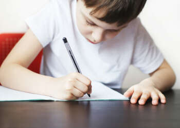 the boy sits at the table and writes in a notebook. child sits and does homework on a white background